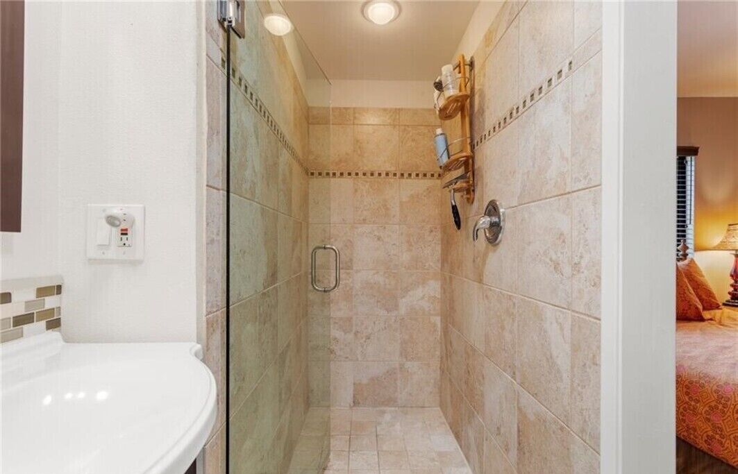 A shower with a glass door, a white sink, and a shelf with toiletries.