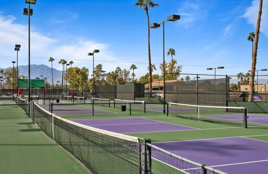 Un court de tennis comprenant plusieurs terrains, entouré de palmiers et avec une montagne en arrière-plan.