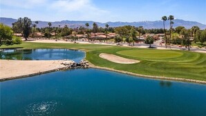 A golf course with a pond, palm trees, and mountains in the background. - Peaceful Waterfront Getaway (pet-friendly) (Palm Desert)