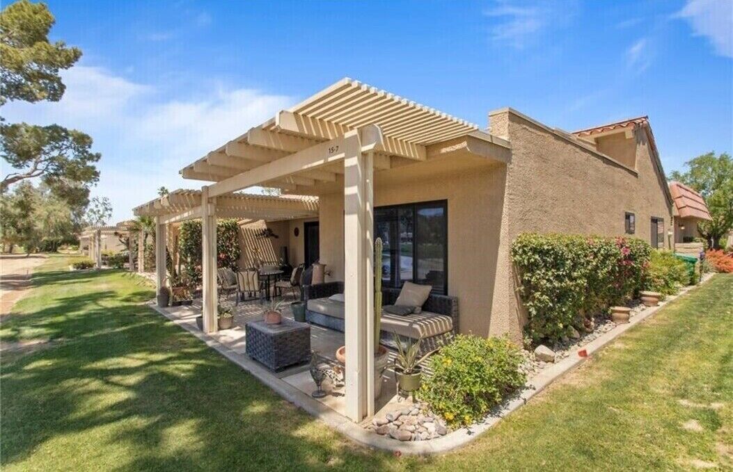 Un área de estar al aire libre cubierta con una pérgola, un patio con mobiliario exterior y un jardín bien cuidado.