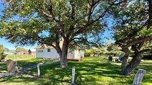 Ein ländliches Anwesen mit einem großen Baum, einem kleinen weißen Haus und einem eingezäunten Garten.