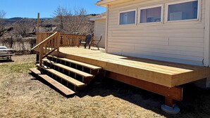 Ein Haus mit einer Holzterrasse, einer Treppe, die zur Terrasse führt, und Blick auf die umliegende Landschaft.