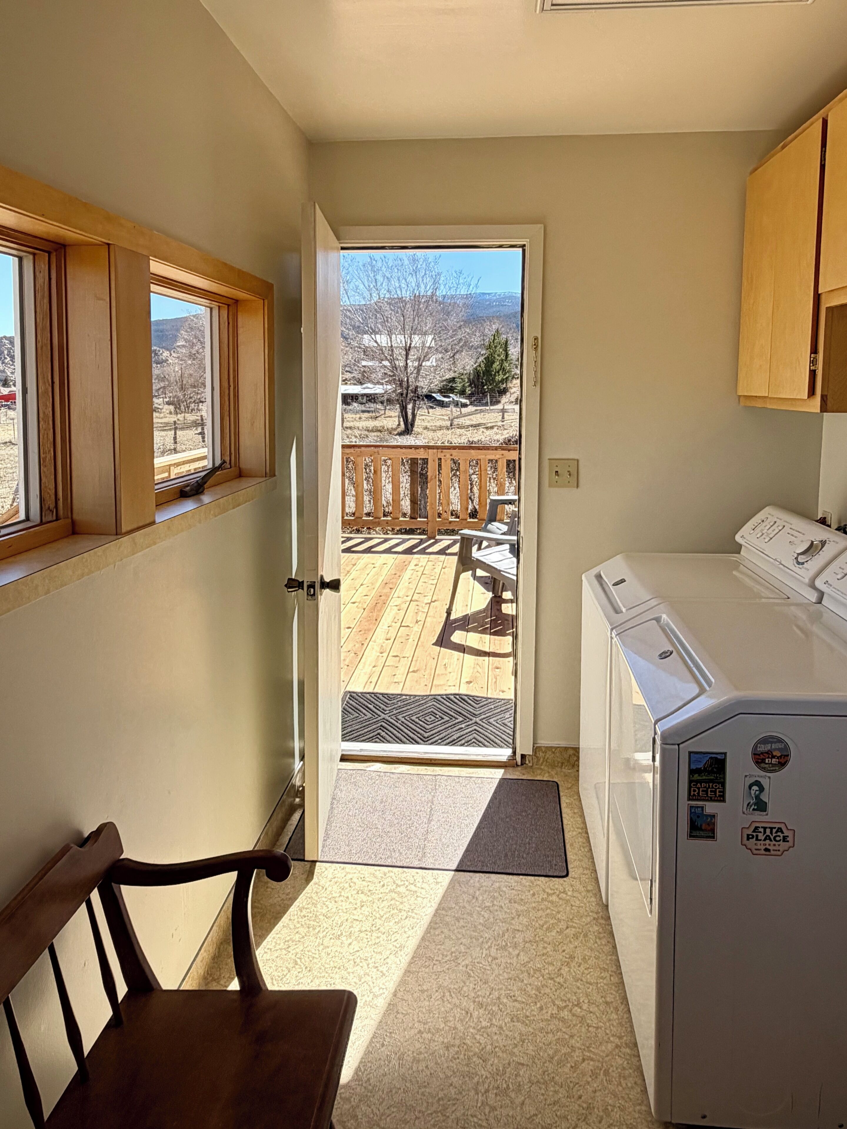 A room with a wooden bench, a washing machine, a door leading to a balcony with a view of a mountainous landscape.