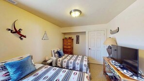 A bedroom with two beds, a television, a wardrobe, and a door leading to another room.