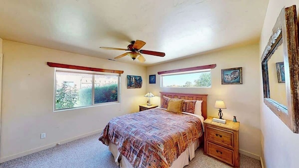 A bedroom with a bed, bedside tables, a ceiling fan, and windows.