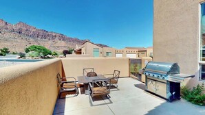 Un patio exterior con una parrilla, una mesa con sillas y vistas a una cadena montañosa.