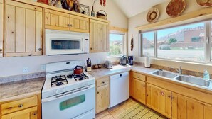 Una cocina con gabinetes de madera, estufa a gas, microondas y pileta.