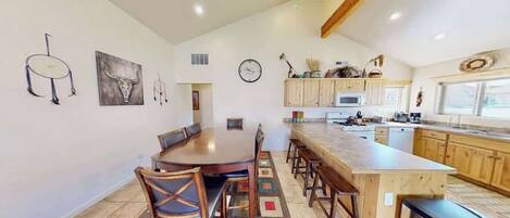 Una cocina amplia con una isla central, armarios de madera y una zona de comedor con sillas.