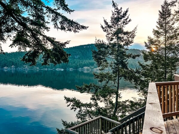 Una terraza de madera con vistas a un lago tranquilo y un bosque denso al fondo.