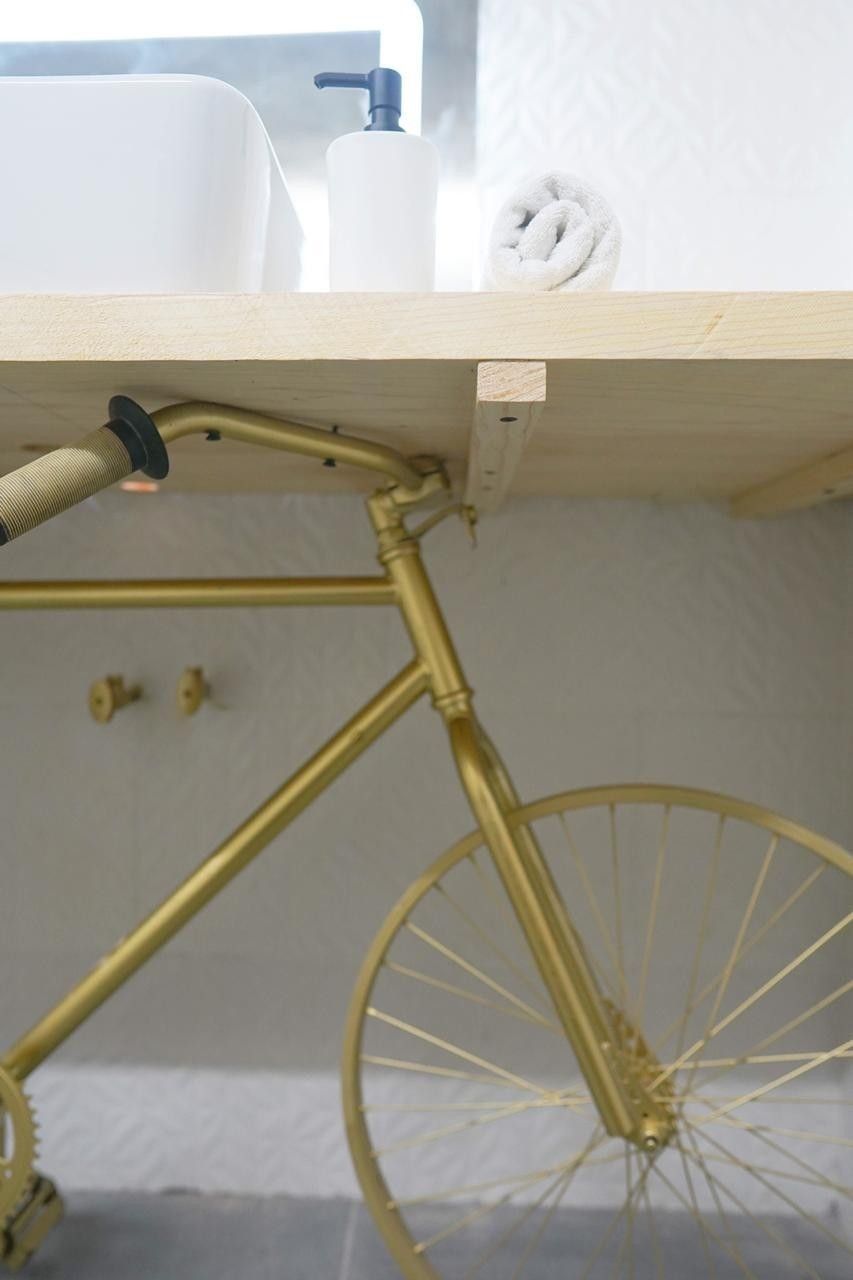 A bicycle under a wooden shelf with a white sink and a towel.
