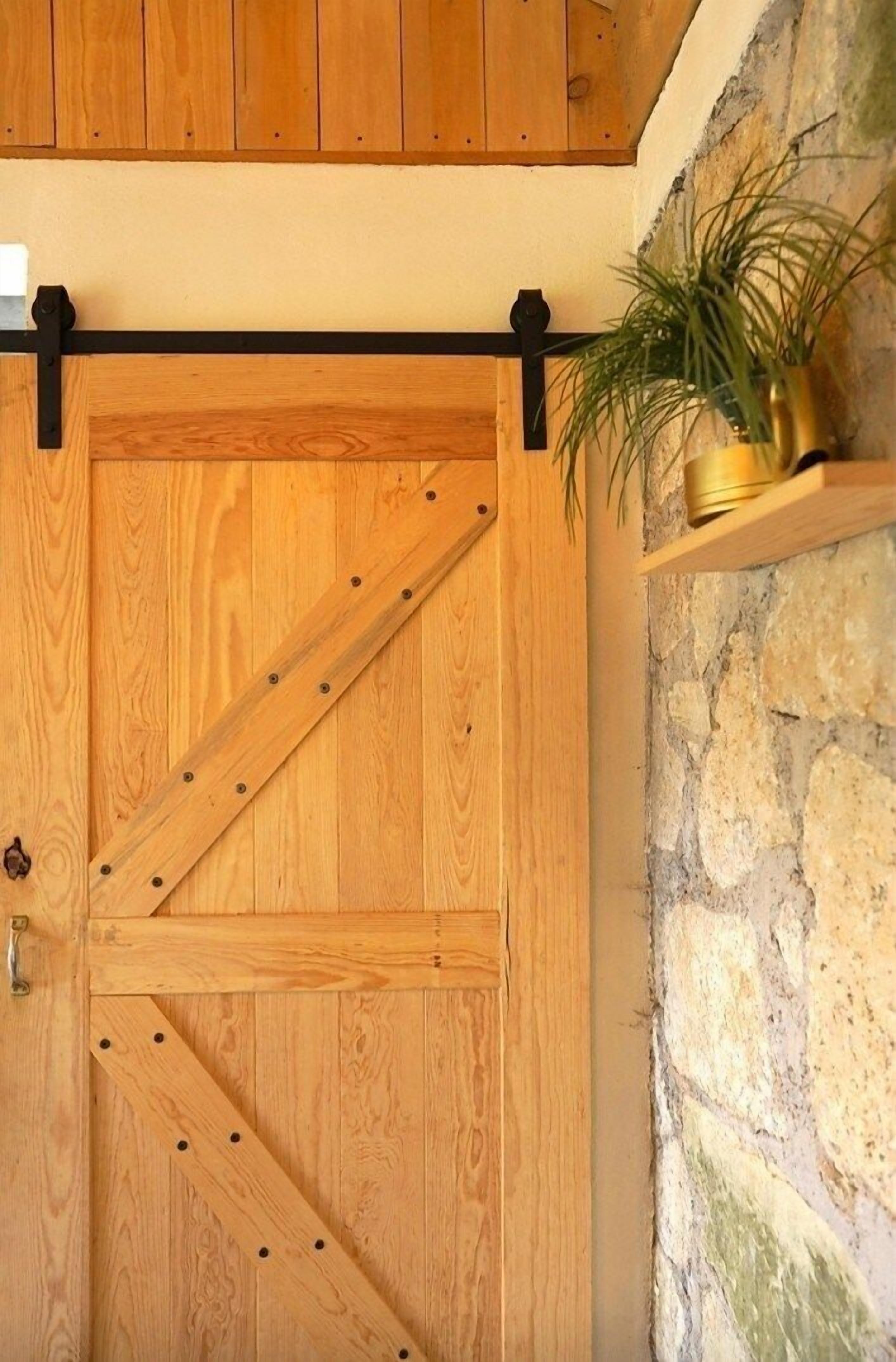 Une porte de grange coulissante en bois, dotée de ferrures métalliques, un mur en pierre et une plante en pot posée sur une étagère.