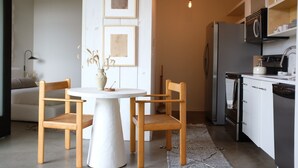 Eine kompakte Küche mit weißen Schränken, einem Einbauofen und einem Geschirrspüler. Es gibt einen Essbereich mit einem weißen Tisch und Holzstühlen.