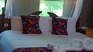 Cama bem arrumada com lençóis brancos, duas almofadas decorativas com padrão vermelho e preto, e um par de toalhas brancas dobradas ao centro.