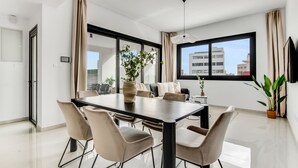 Una sala de estar moderna con una mesa de comedor, sillas color beige, una planta en maceta y un ventanal con vista a la ciudad.