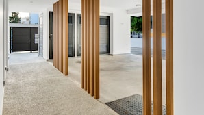 Un couloir moderne avec un sol en béton, des panneaux verticaux en bois et une porte en métal ornée d’un panneau indiquant un espace de stationnement.