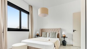 Une chambre moderne avec un grand lit, deux tables de chevet, un luminaire suspendu et une vue sur la ville grâce à une grande fenêtre.