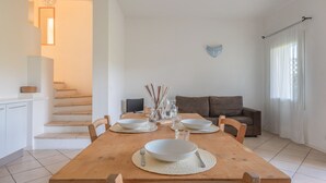 A dining area with a wooden table set for two, a sofa, and a staircase in the background.