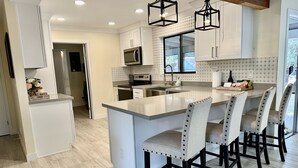 A modern kitchen with a central island, bar stools, and pendant lighting.