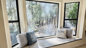 A window seat with three pillows, one with "HOME SWEET HOME" text, and a view of a forested area.