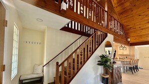 A wooden staircase with intricate designs, a bench, a potted plant, and a kitchen area with bar stools.