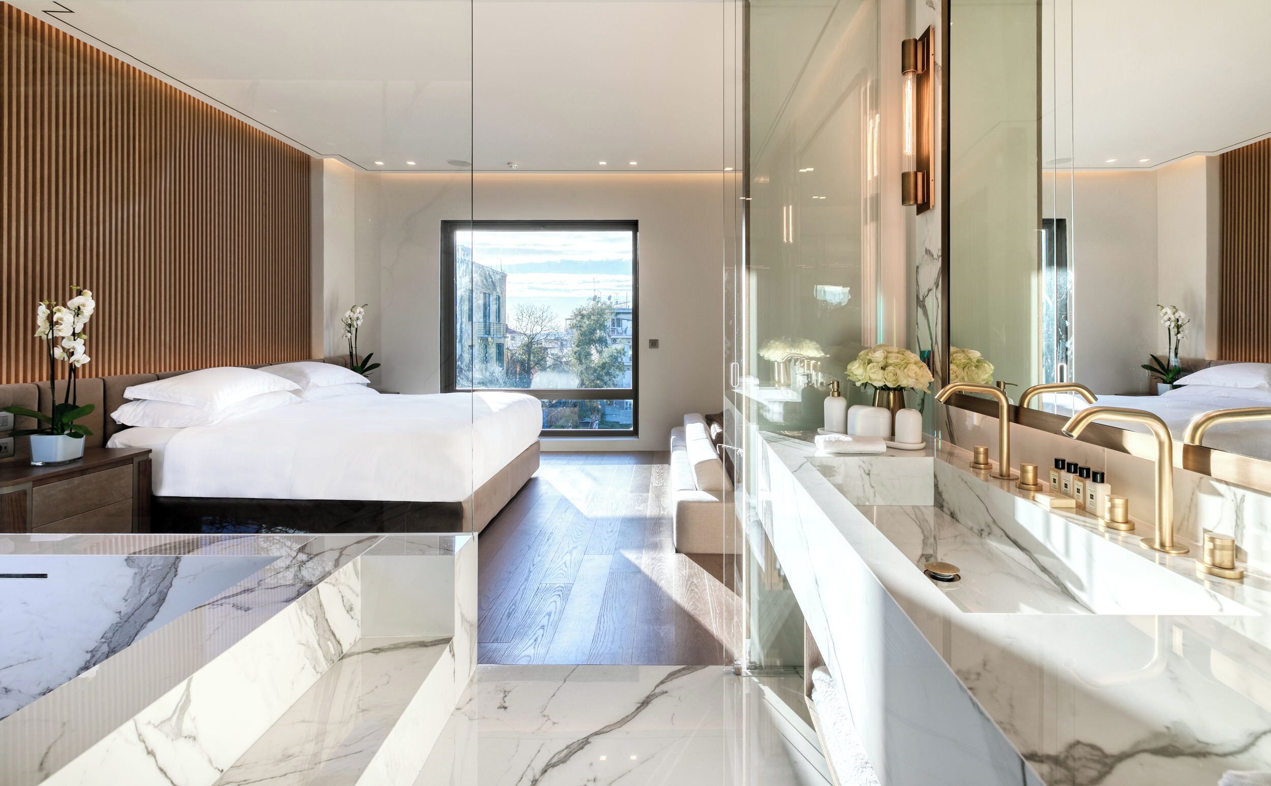 A modern hotel room with a large bed, a glass shower enclosure, and a marble bathroom.