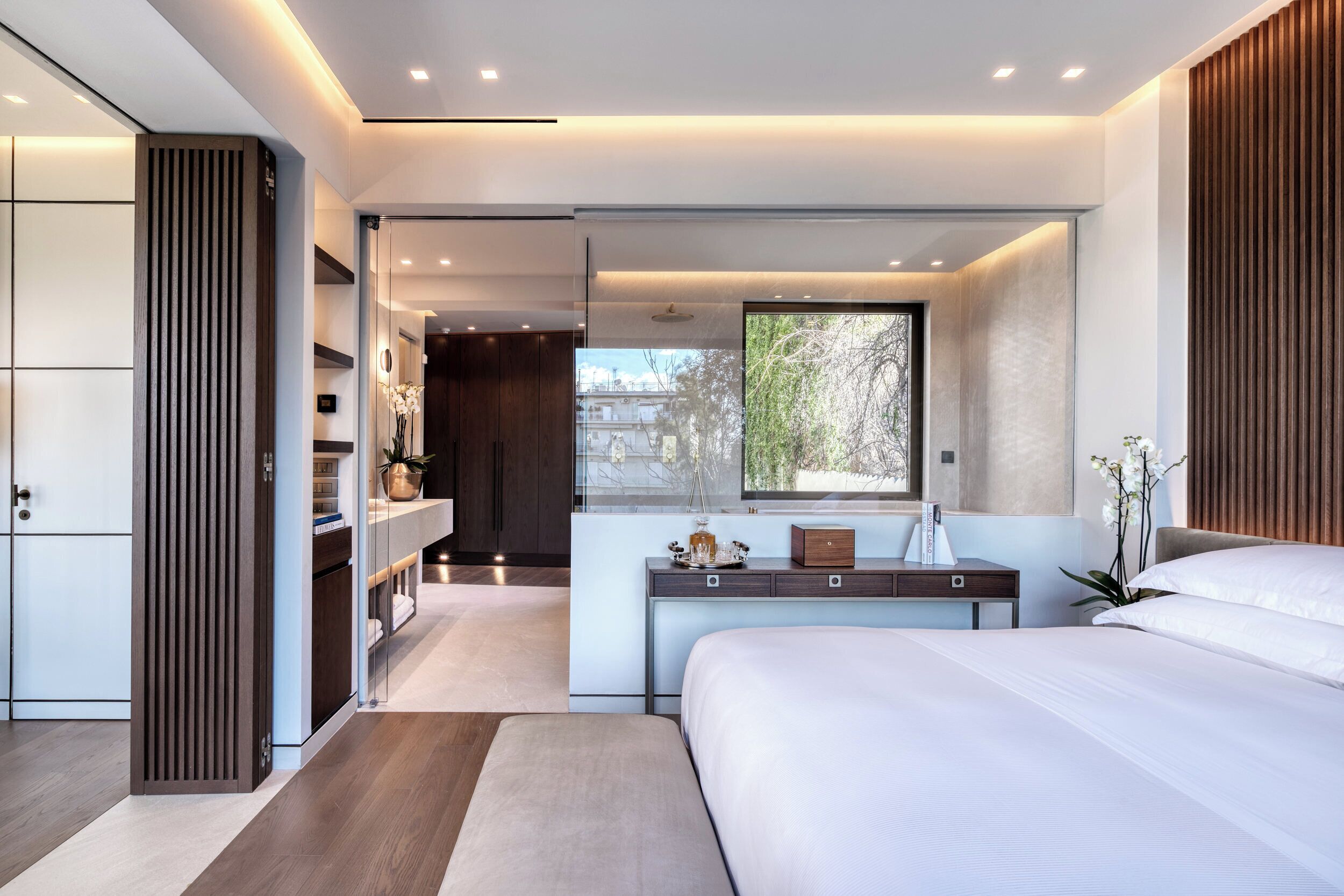 Un dormitorio moderno con una cama grande, mesitas de noche, un armario y una ventana con vistas a árboles.