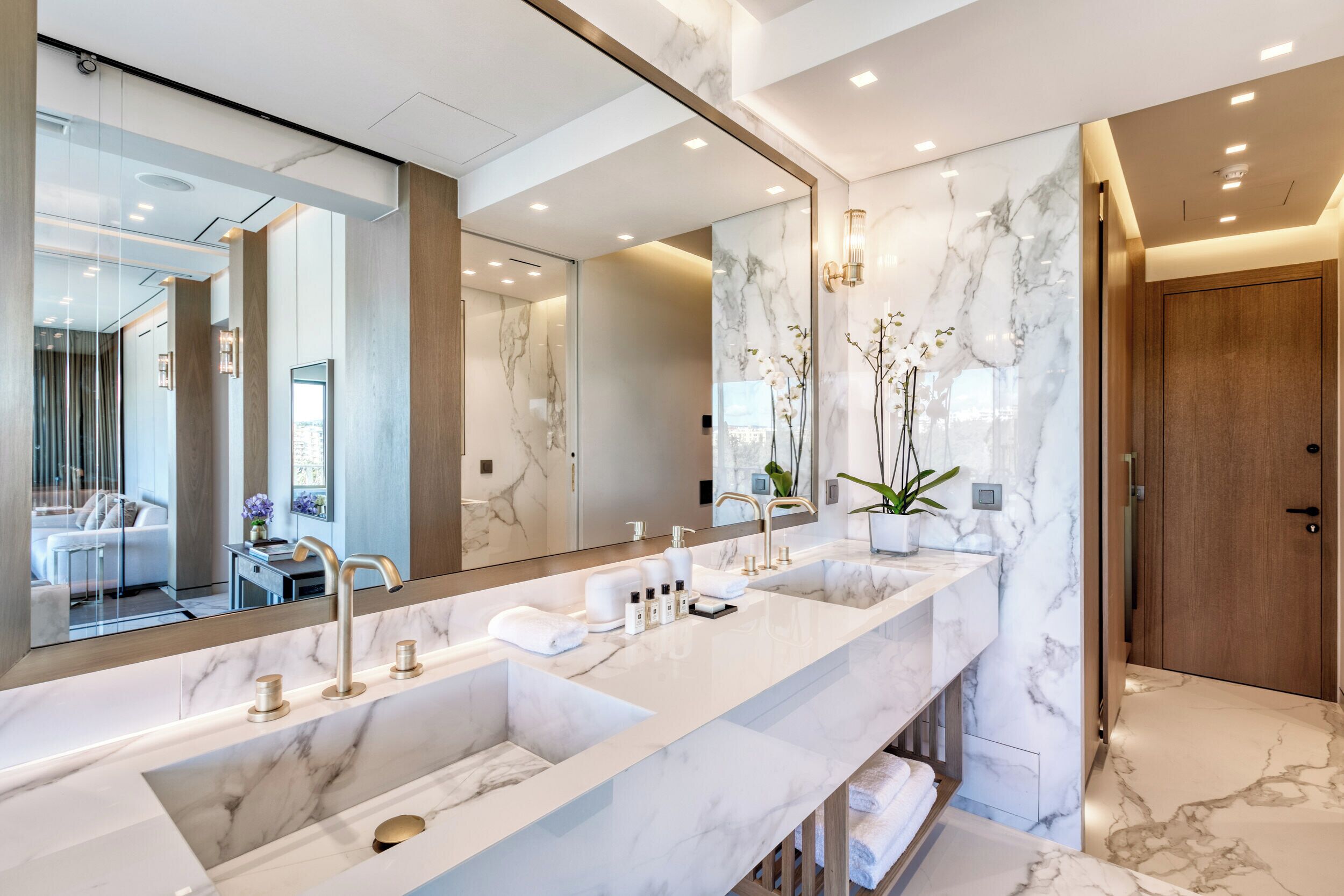 A modern bathroom with two sinks, a large mirror, and marble walls.