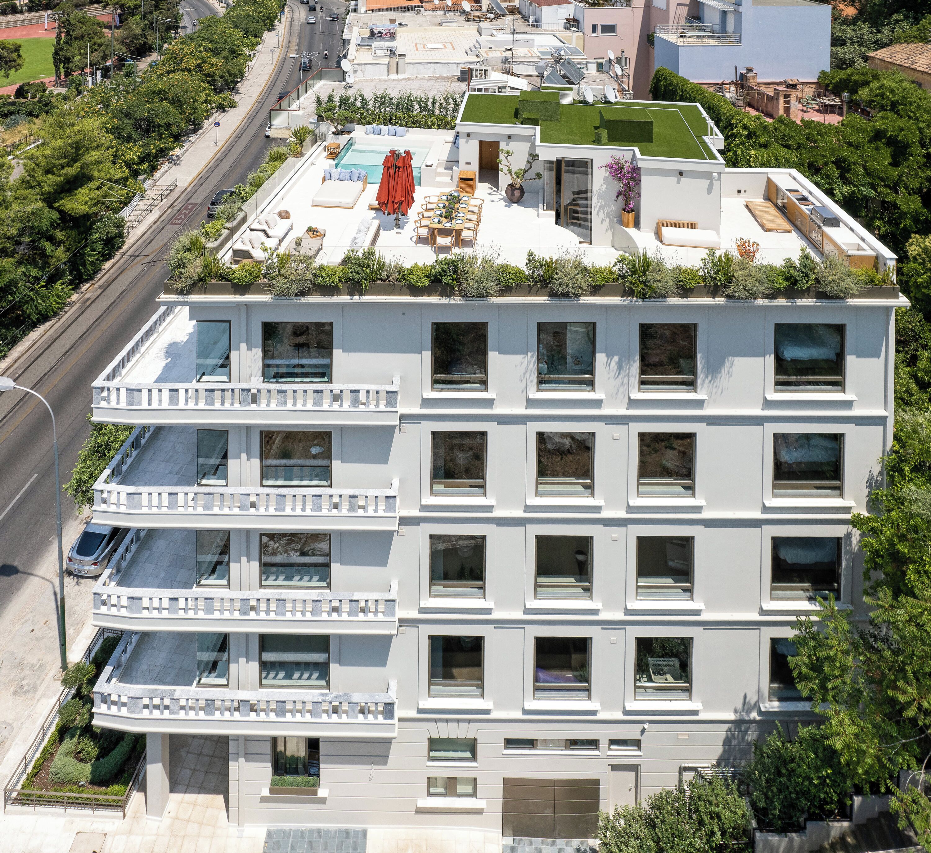 Un edifici modern d'àmbit elevat amb balcons, una piscina al terrat i un teulat verd.