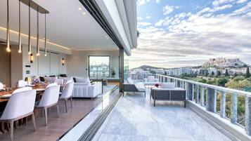 A modern living room with a dining area, large windows, and a balcony with a city view.