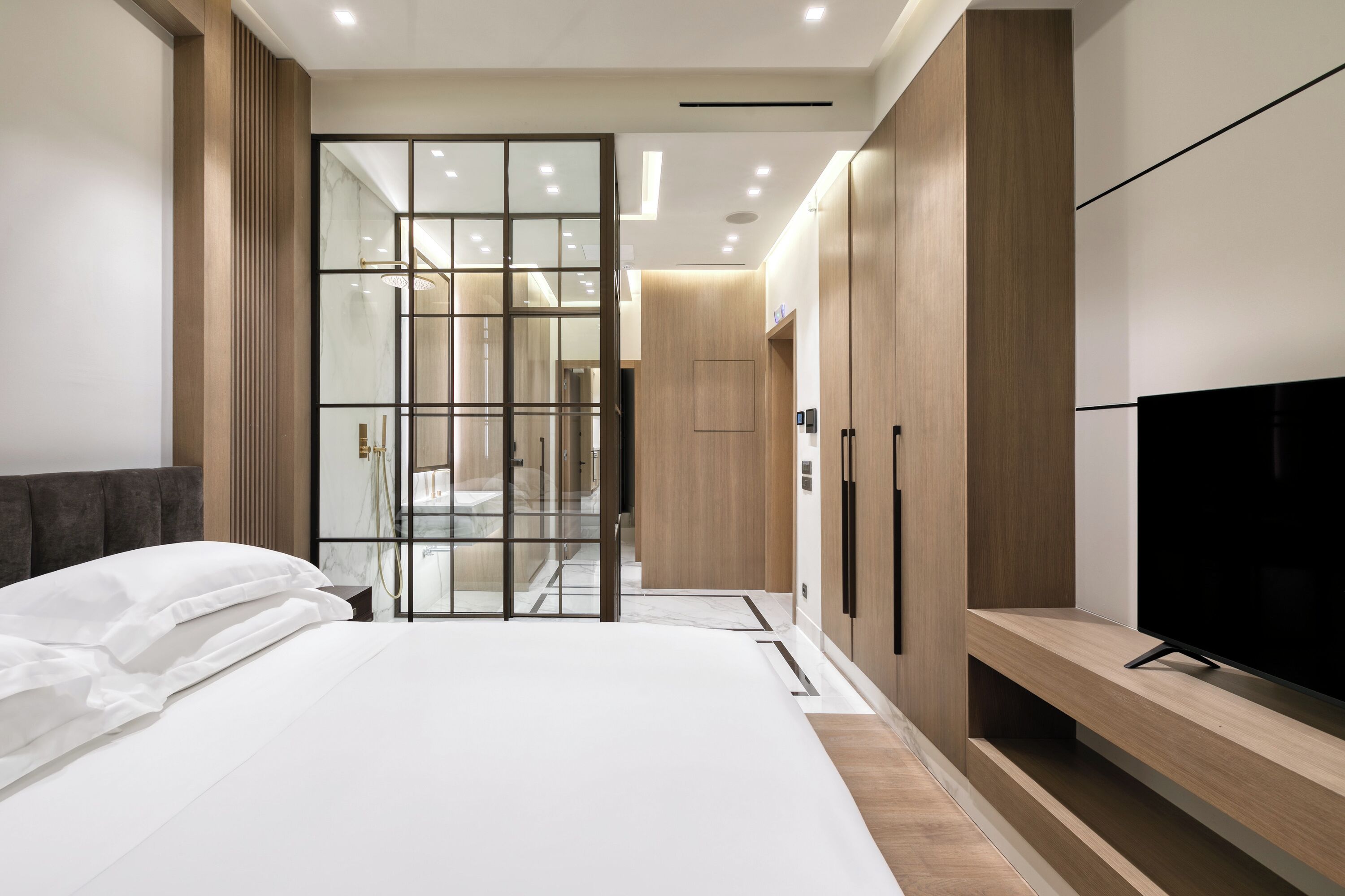A modern bedroom with a large bed, a TV on a wooden stand, and a wardrobe with a mirror.
