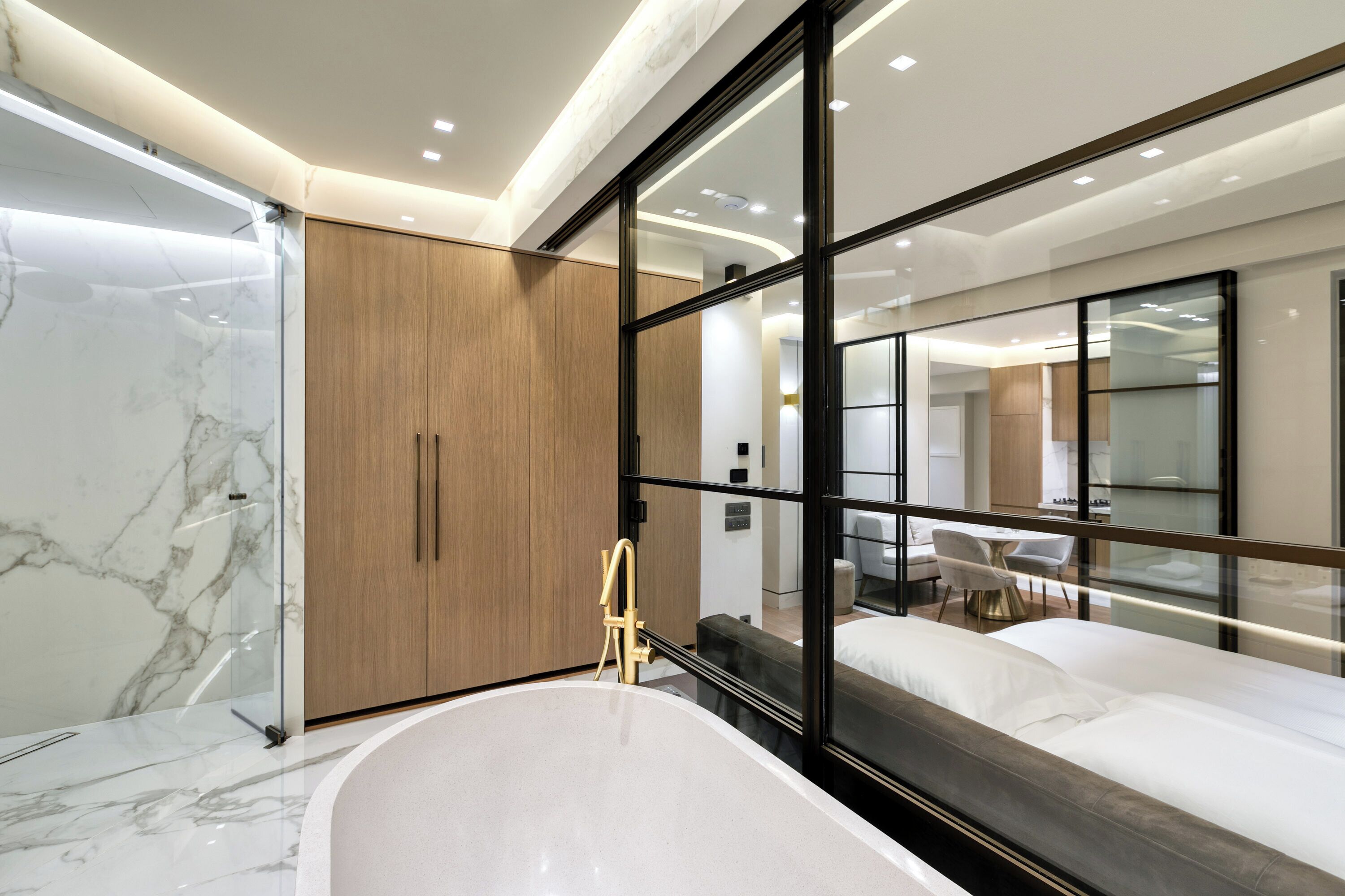Un baño moderno con ducha de mármol, armario de madera y zona de descanso con cama, todo ello separado por vidrio.