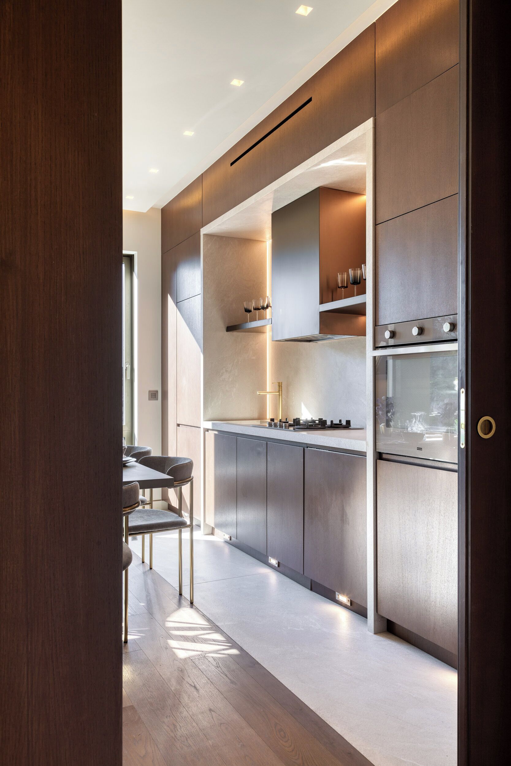 A modern kitchen with built-in appliances, a dining area with chairs, and a wooden floor.