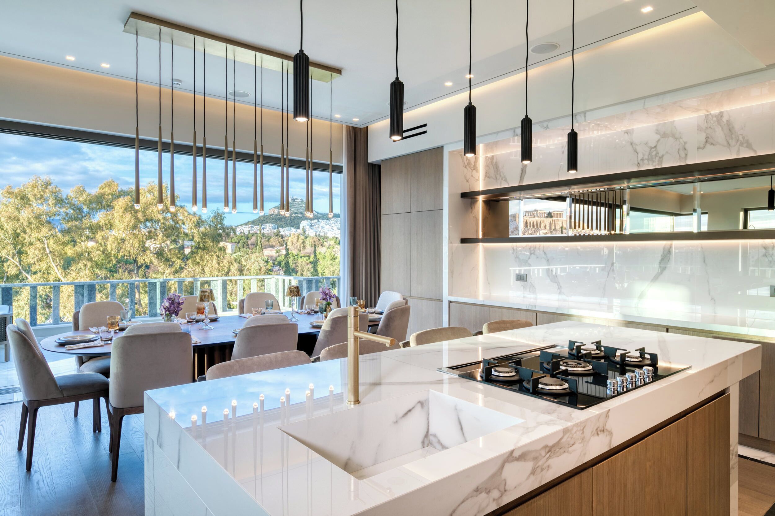 Une cuisine moderne dotée d’un grand îlot central, de luminaires suspendus et offrant une vue sur l’extérieur.