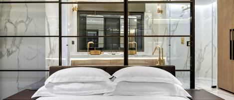 A modern bedroom with a large bed, a glass-enclosed bathroom, and marble walls.