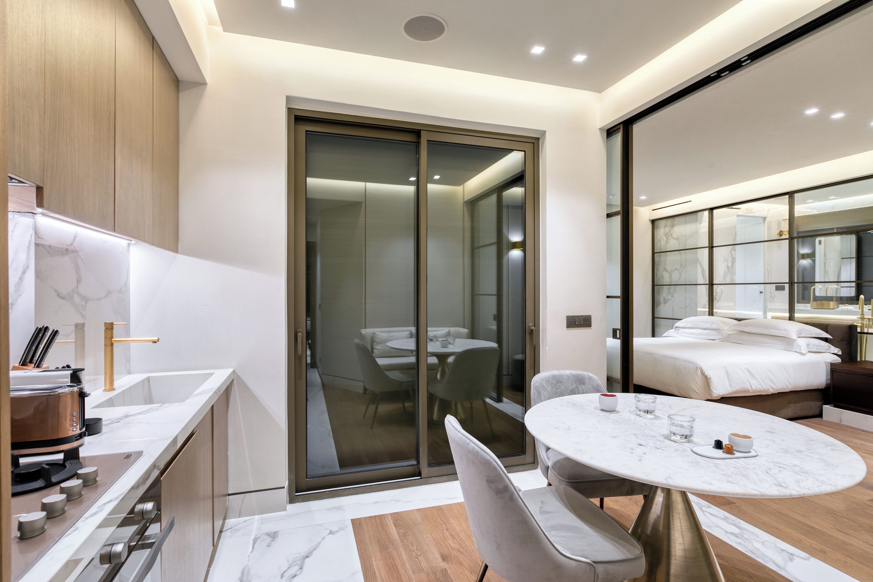 A modern hotel room with a marble bathroom, a dining area, and a bedroom with a large bed and a nightstand.
