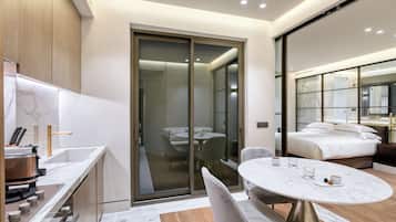 A modern hotel room with a marble bathroom, a dining area, and a bedroom with a large bed and a nightstand.