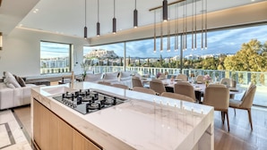 Una cocina moderna con una isla grande, comedor con sillas y vista a un paisaje urbano.