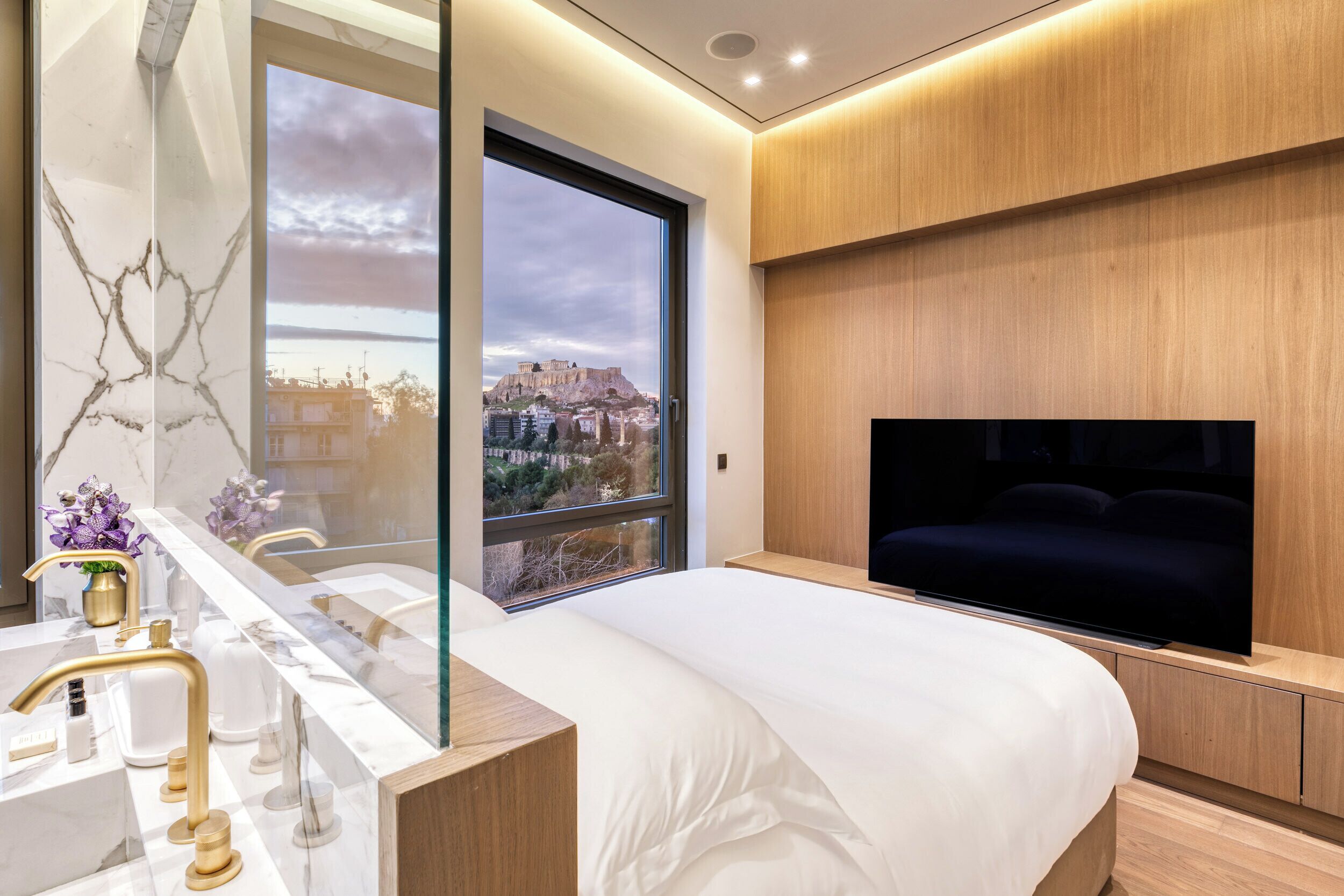 A modern bedroom with a large bed, a TV, a marble vanity, and a view of a historic building.