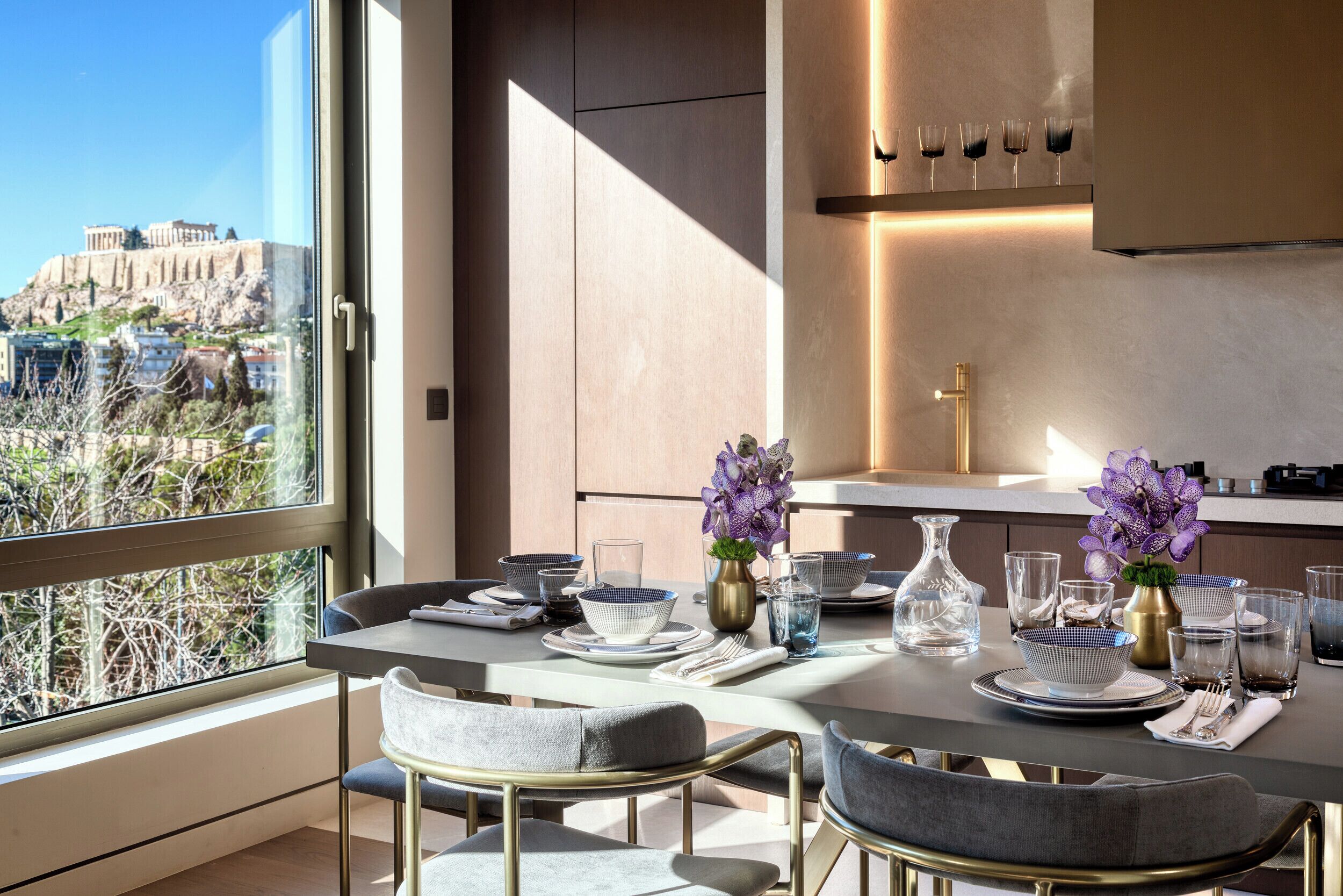 Un espace de restauration moderne avec une table dressée pour quatre personnes, une vue sur l’Acropole et un aménagement intérieur minimaliste.