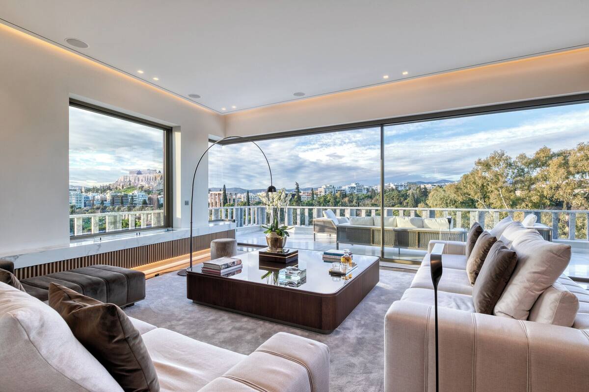 A modern living room with a large window, a sofa, a coffee table, and a view of a cityscape.