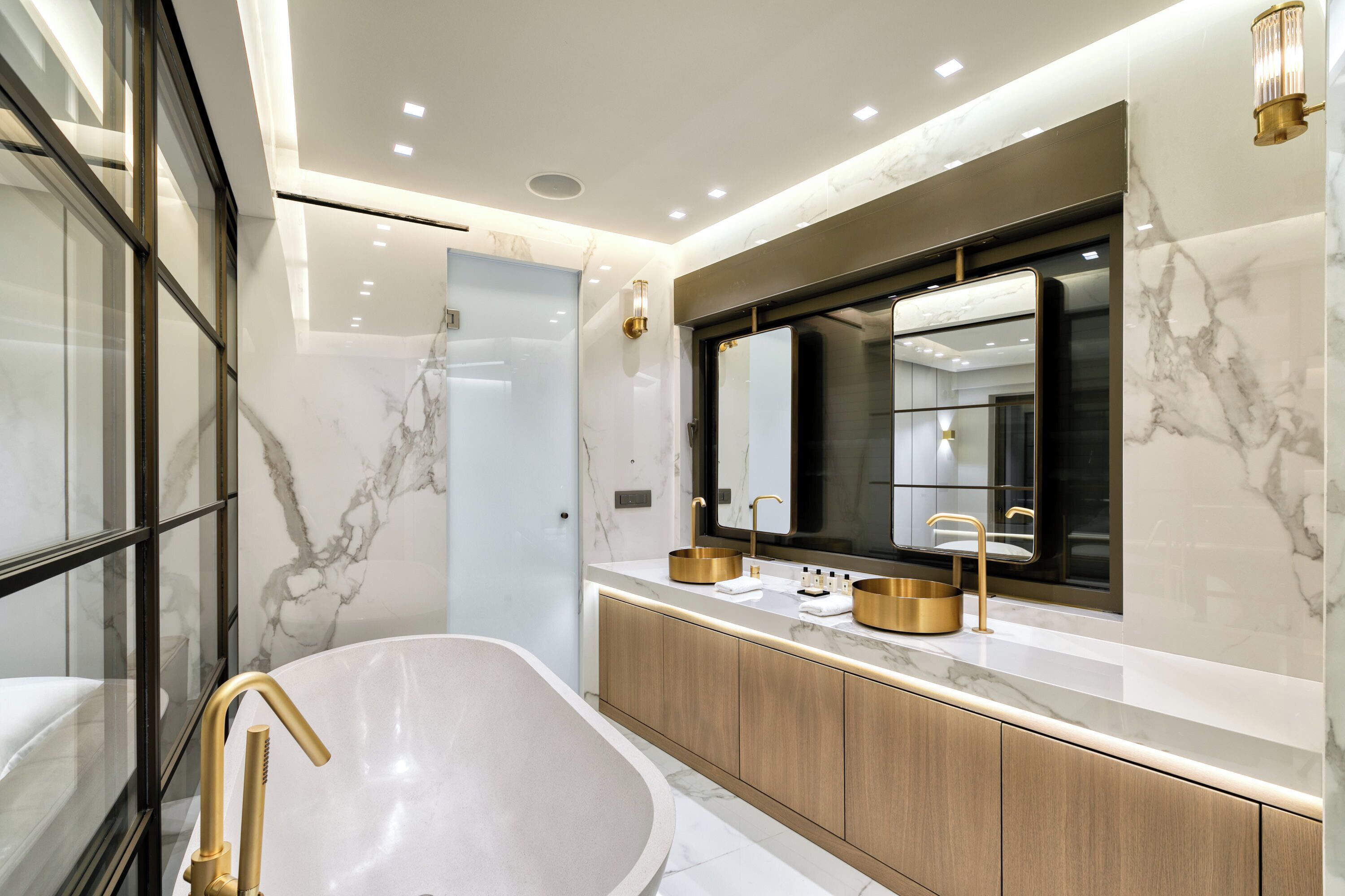A modern bathroom with a freestanding bathtub, a large mirror, and marble walls.