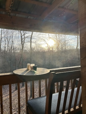 A wooden deck with a table and chairs, overlooking a forested area with bare trees and a clear sky.