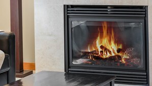 Una chimenea moderna con fuego a la vista, un control remoto sobre una mesa y un sofá de cuero.