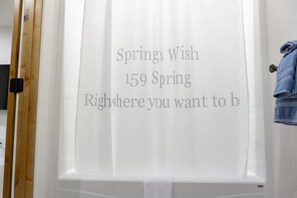Un baño con cortina de ducha que muestra 'Springs Wish 159 Spring' y un perchero con una toalla azul.
