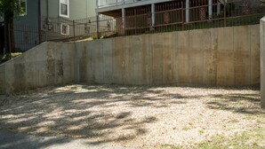 A concrete retaining wall with a gravel surface, a metal fence, and a residential building in the background. - Downtown Historic Loop Downstairs Queen Free Parking (Eureka Springs)