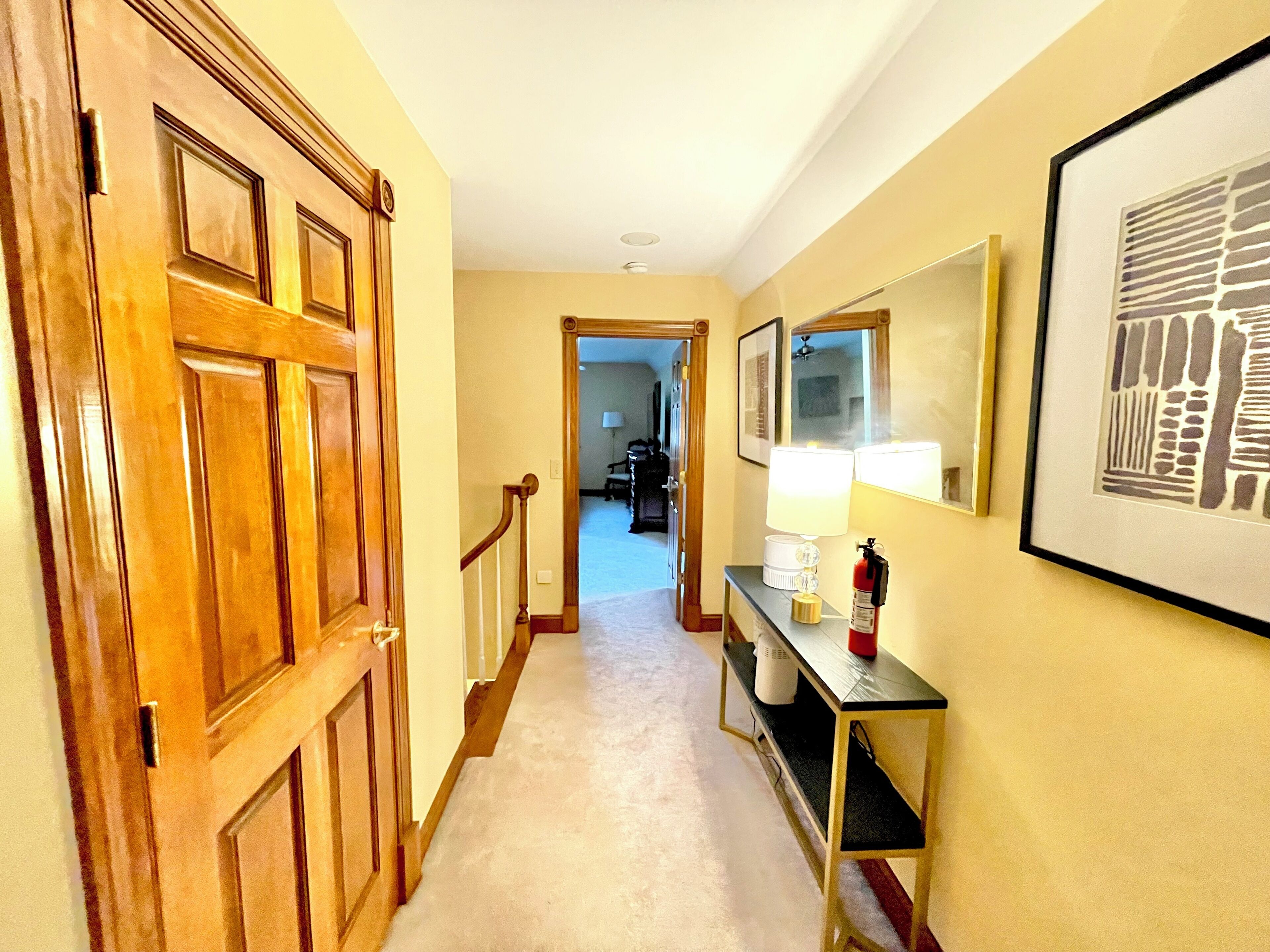 A hallway with a wooden door, a console table with a lamp, a framed picture, and a fire extinguisher.