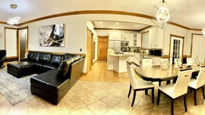 A modern living room with a black leather sofa, a dining area with a round table and chairs, and a kitchen with white cabinets and a microwave. - Huge Farmstay w/ Pool, Animals, Pond, Event Barn, & Clubhouse w/ Game Room (La Plata)