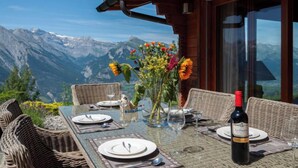 Una mesa de comedor al aire libre con vistas a la montaña, sillas de mimbre y una botella de vino.