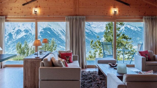 Una cabaña acogedora con paredes de madera, un sofá, una mesa y vistas a montañas nevadas.
