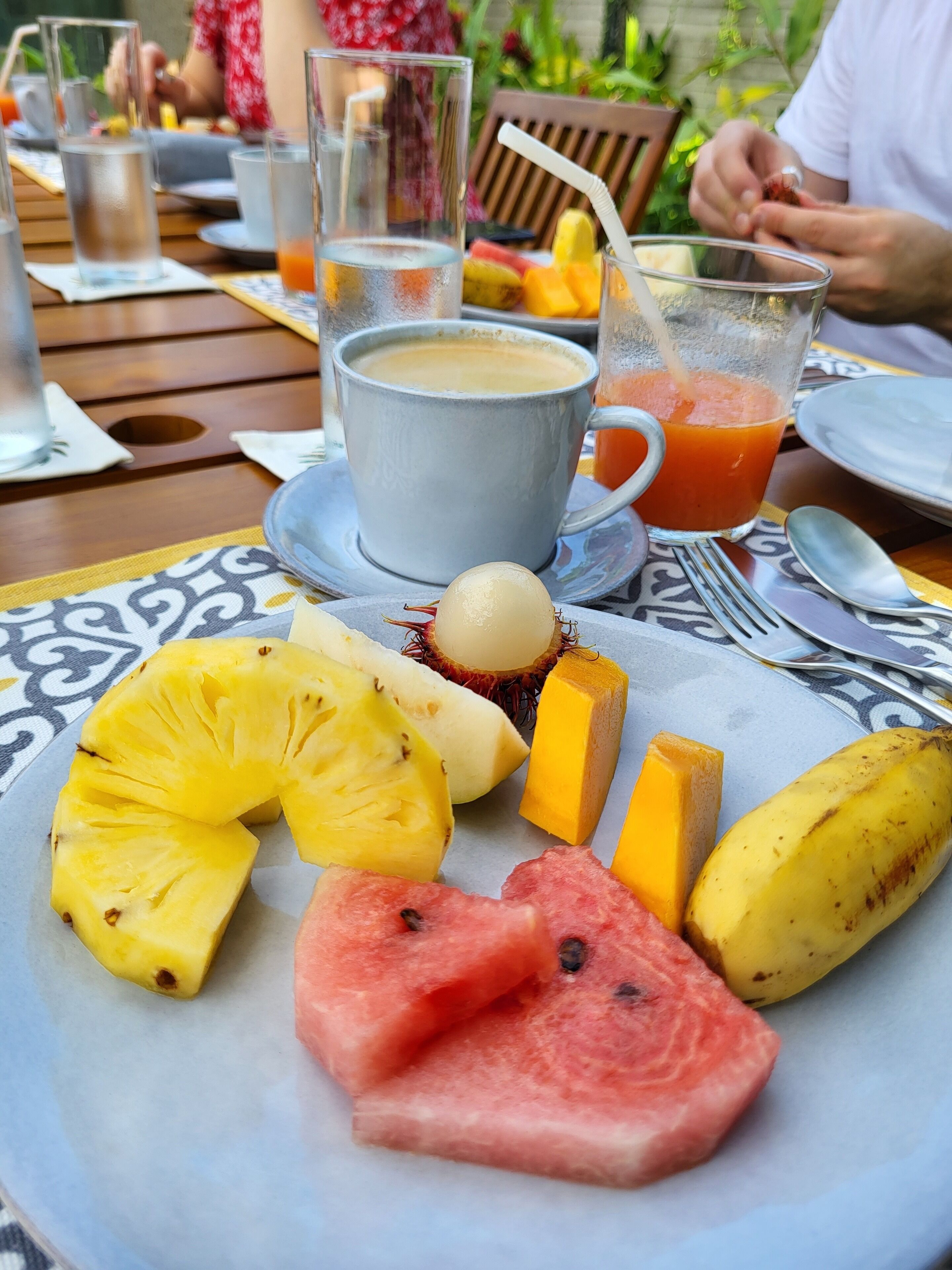A dining table with a plate of fruit, a cup of coffee, and a glass of juice.